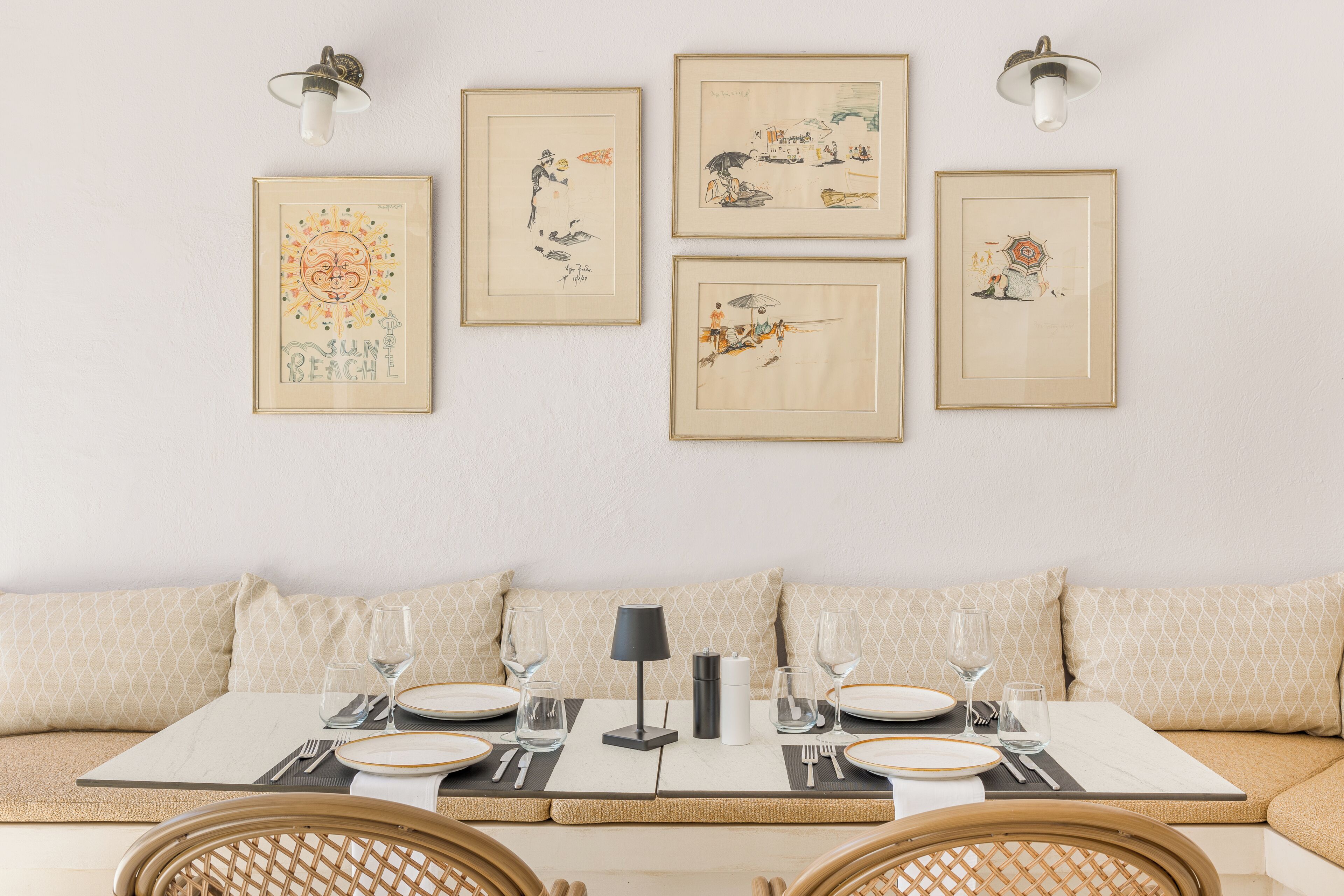 A dining area with a table set for two, a sofa with patterned cushions, and wall-mounted artwork.