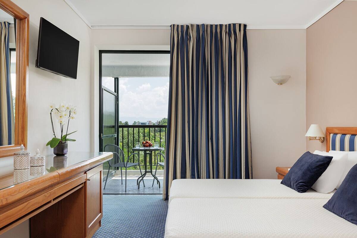 A hotel room with a bed, a desk, a TV, a balcony with a table and chairs, and a view of the outside.