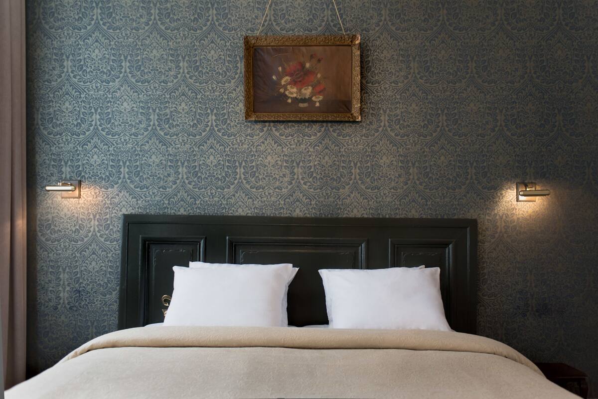 A neatly made bed with a dark headboard and two white pillows, set against a patterned wallpaper.