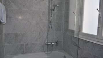 Un baño moderno con ducha envuelta en vidrio, una bañera y un revestimiento de mármol.
