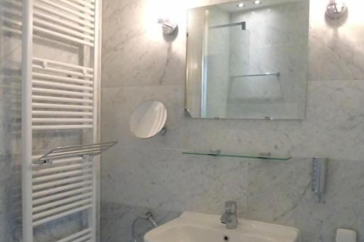 Une salle de bain avec un lavabo blanc, une cabine de douche en verre, un porte-serviettes et une poubelle.