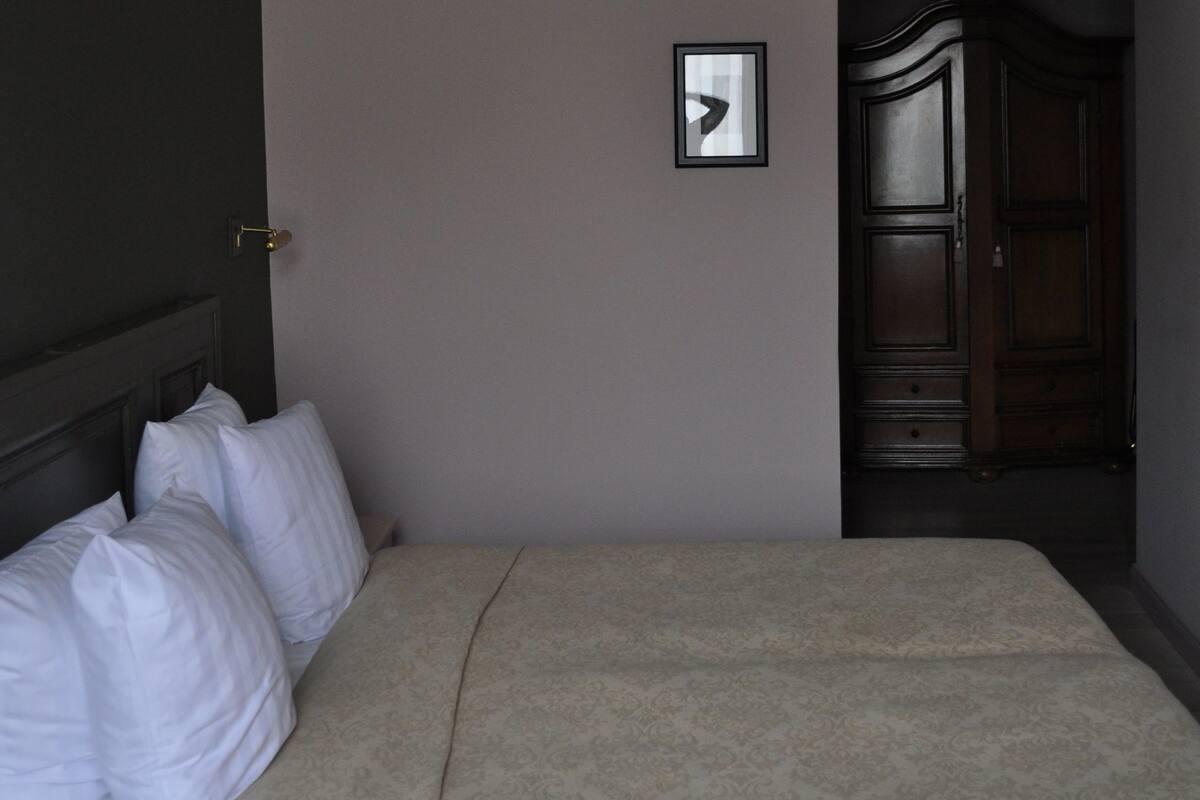 A bedroom with a bed, a chandelier, a door, and a framed picture on the wall.