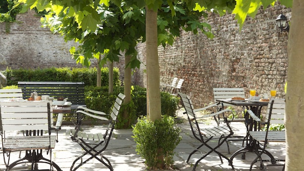Un patio al aire libre con suelo de piedra, bancos y mesas de metal.