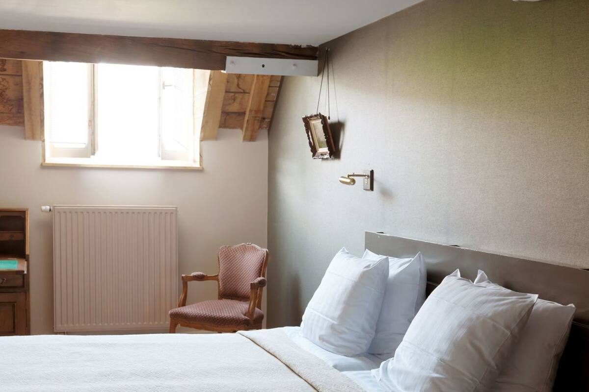 A bedroom with a bed, a chair, a radiator, and a window.