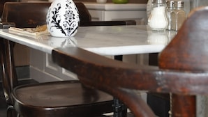 Una mesa de comedor con un jarrón blanco, sillas de madera y una cocina al fondo.
