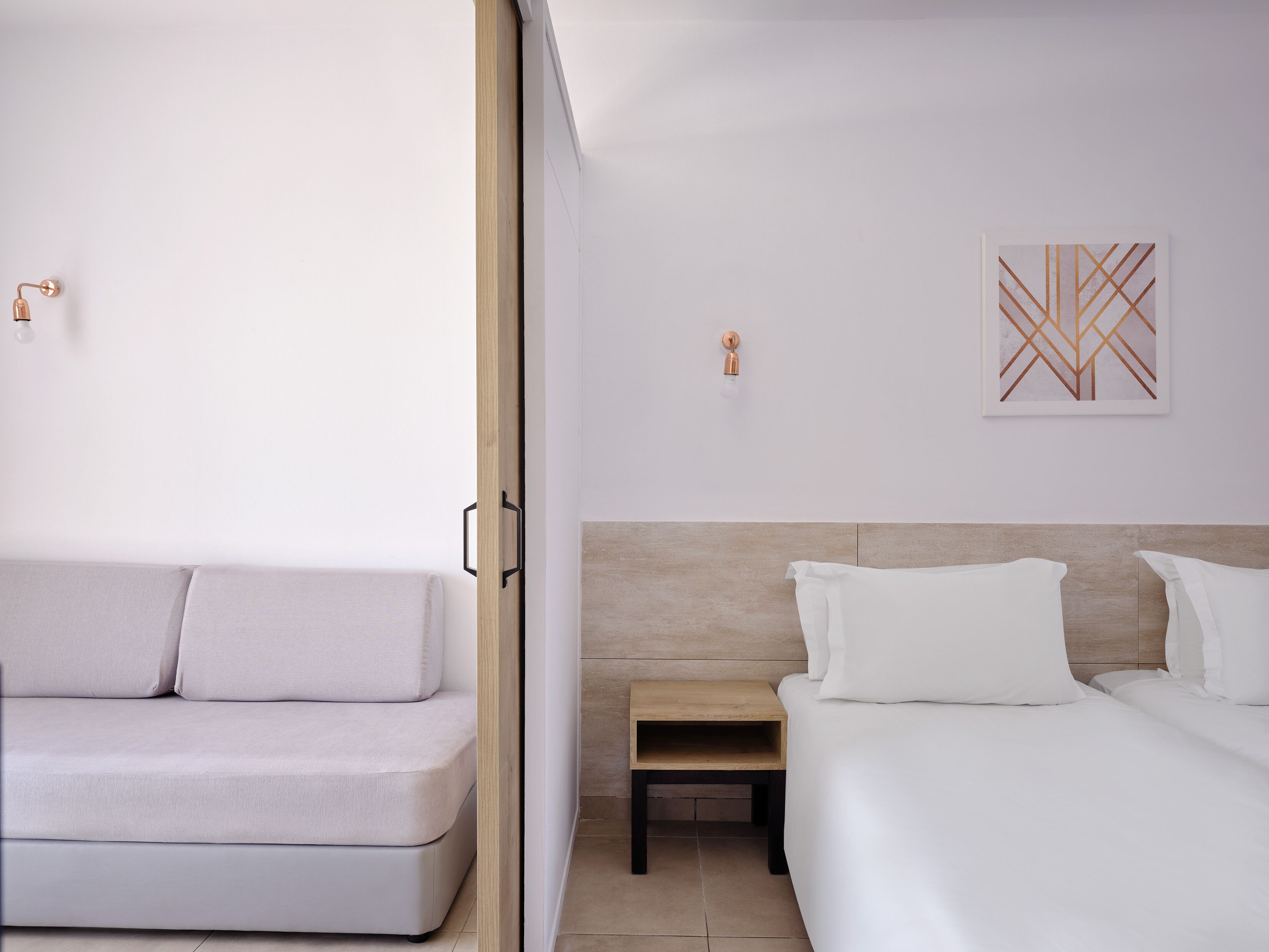 Een moderne hotelkamer met een bank, een bed, een nachtkastje en een wandlamp.