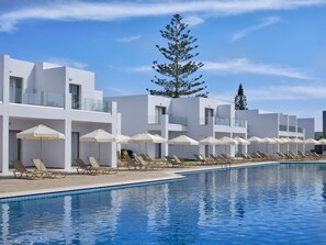 A modern hotel with a pool area, sun loungers, and umbrellas.