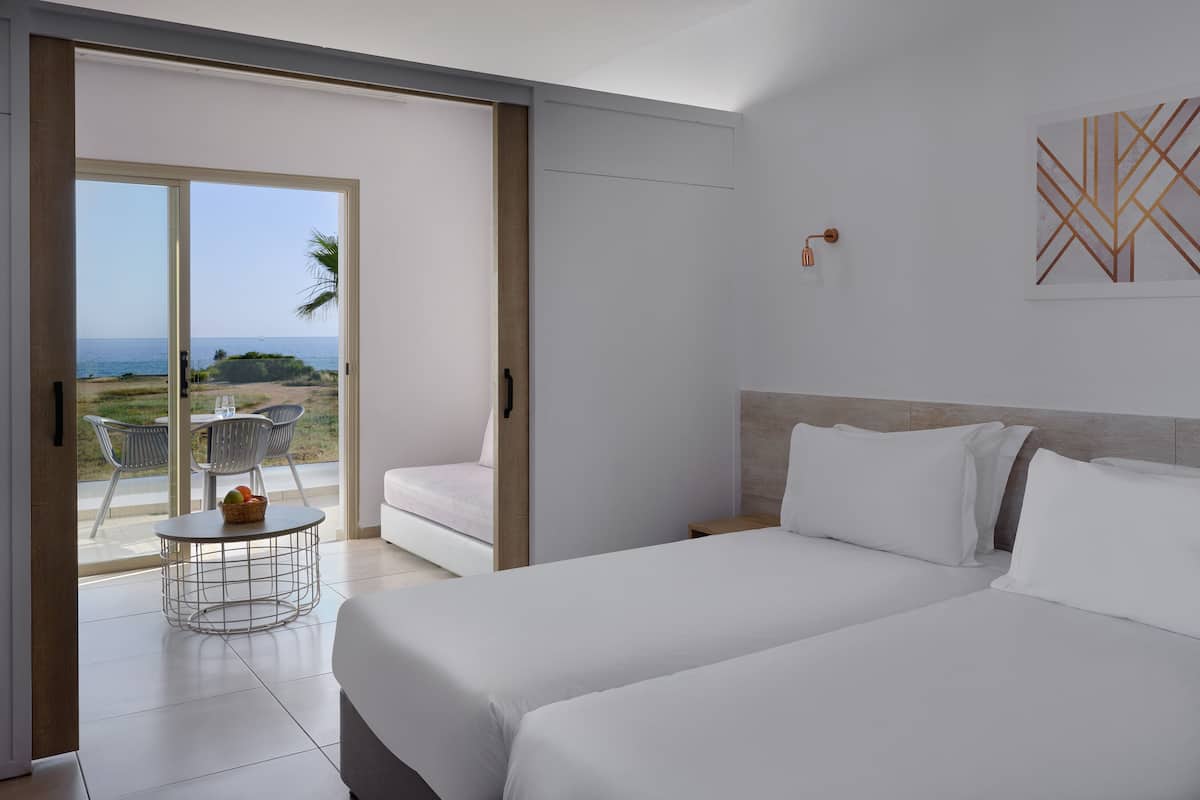 A bedroom with a bed, a nightstand, and a view of the beach through an open door.