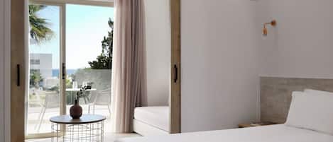 A modern hotel room with a large bed, a round table with a vase, and a balcony with a view of the sea.