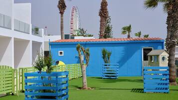 Un parque infantil con estructuras de juego azules, una noria y palmeras.