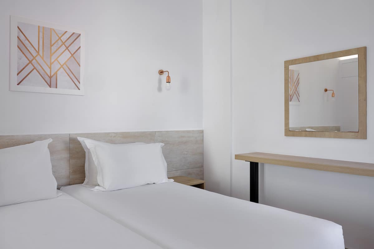 A hotel room with a bed, a nightstand, a wall-mounted mirror, and a wall art piece.