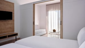 Une chambre d’hôtel moderne avec un grand lit, un téléviseur fixé sur un panneau en bois, un canapé et une petite table avec un panier.
