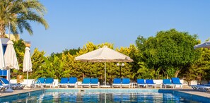A swimming pool with blue lounge chairs and umbrellas, surrounded by greenery.