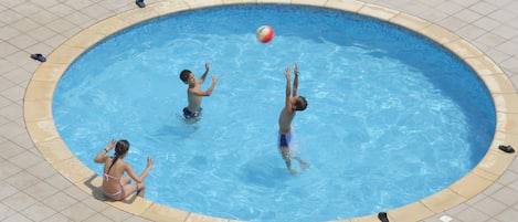 A swimming pool with three people playing with a ball.