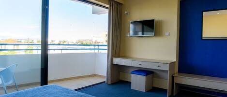 A hotel room with a bed, a desk, a TV, and a view of the city through large windows.