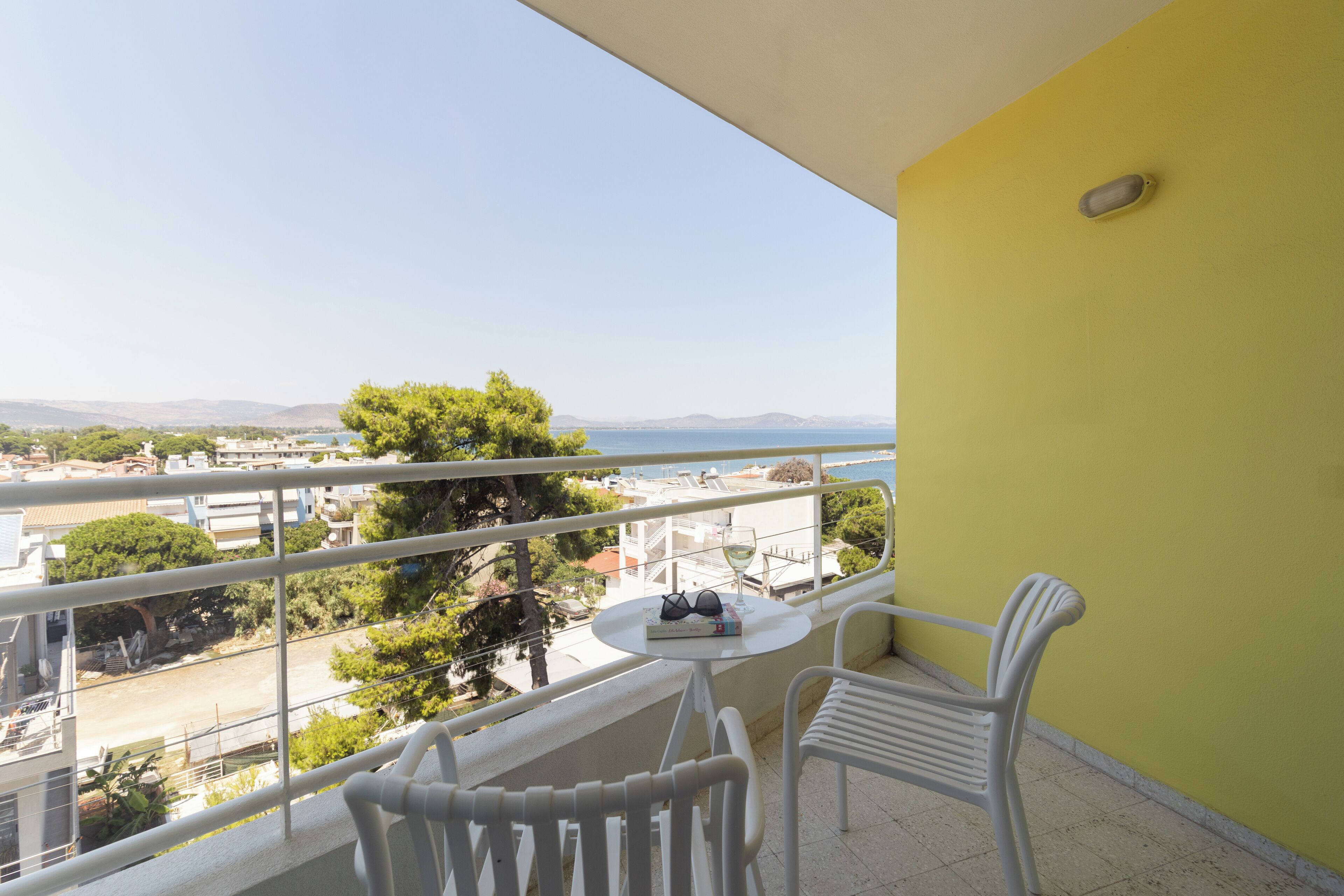 A balcony with a yellow wall, white railing, and two white chairs.