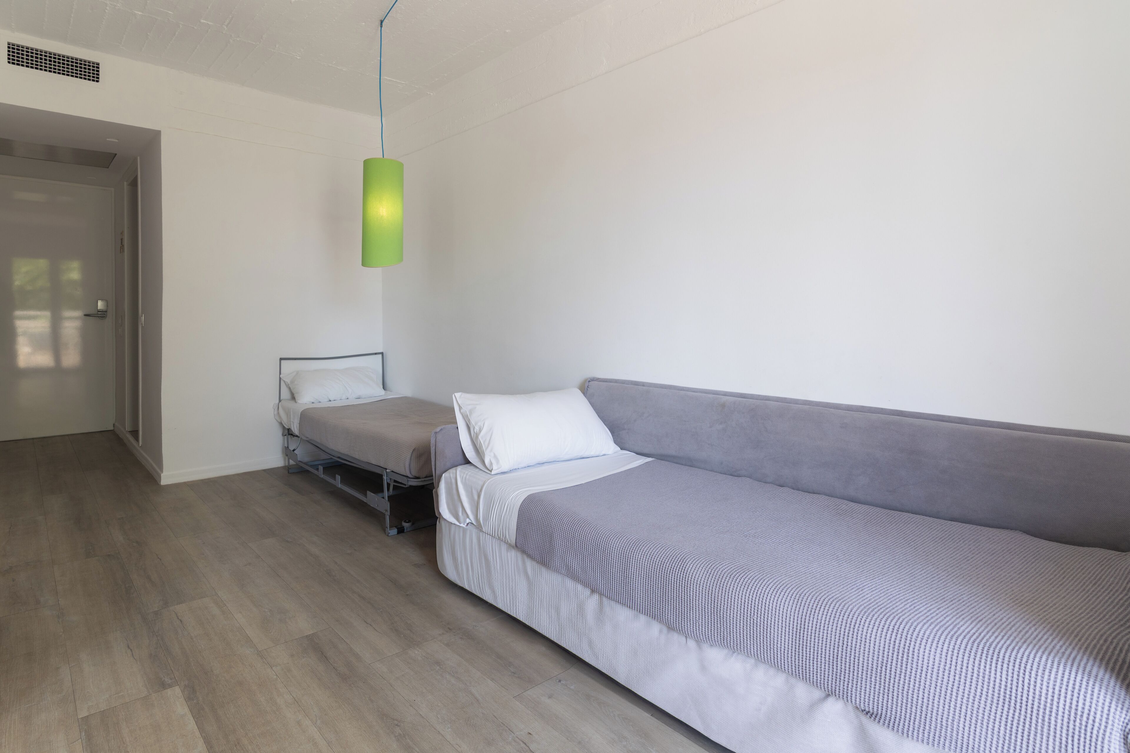 Quarto moderno e minimalista com um sofá cinza, uma cama de solteiro e uma luminária pendente verde.