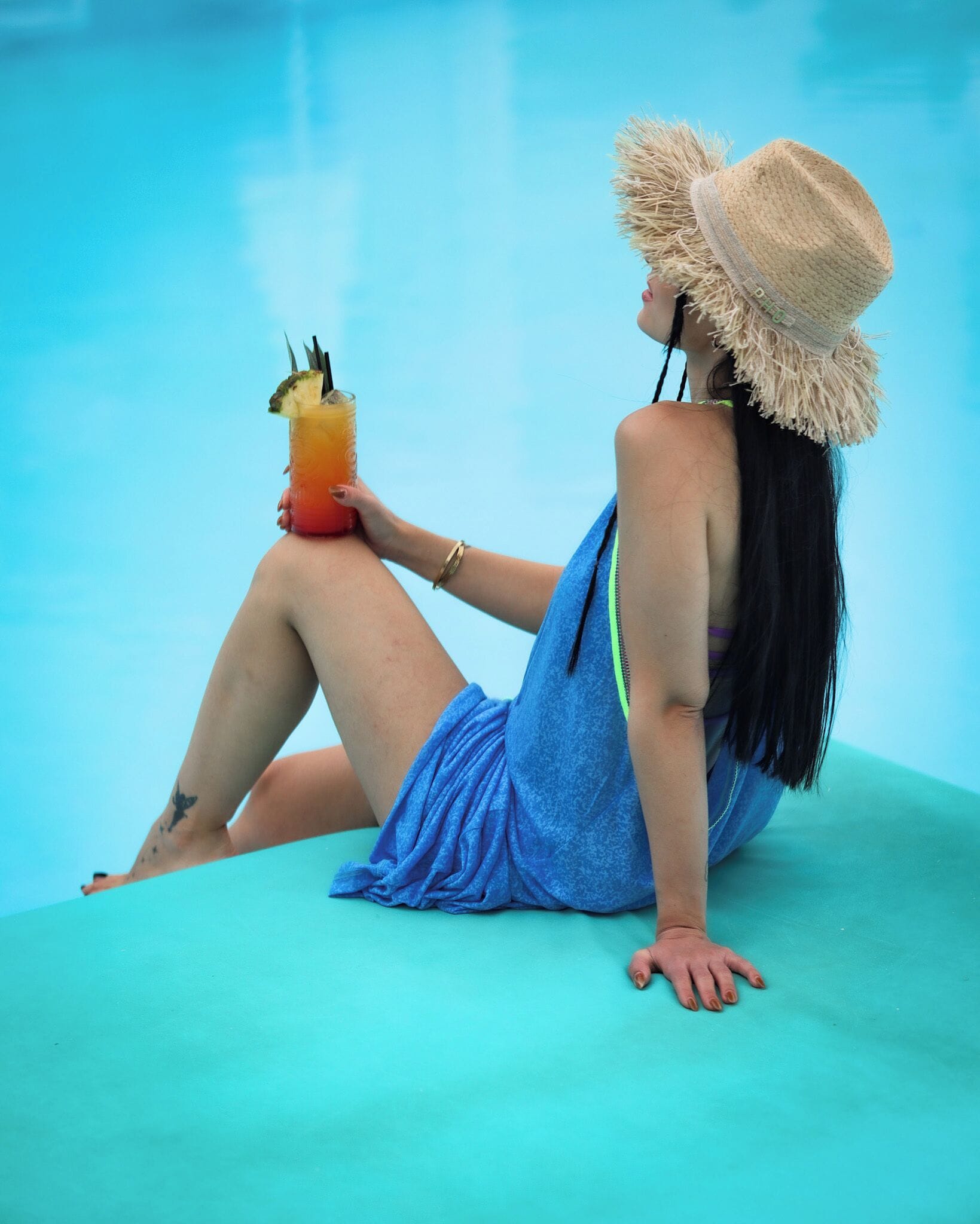 A person sitting by a pool with a drink in hand.
