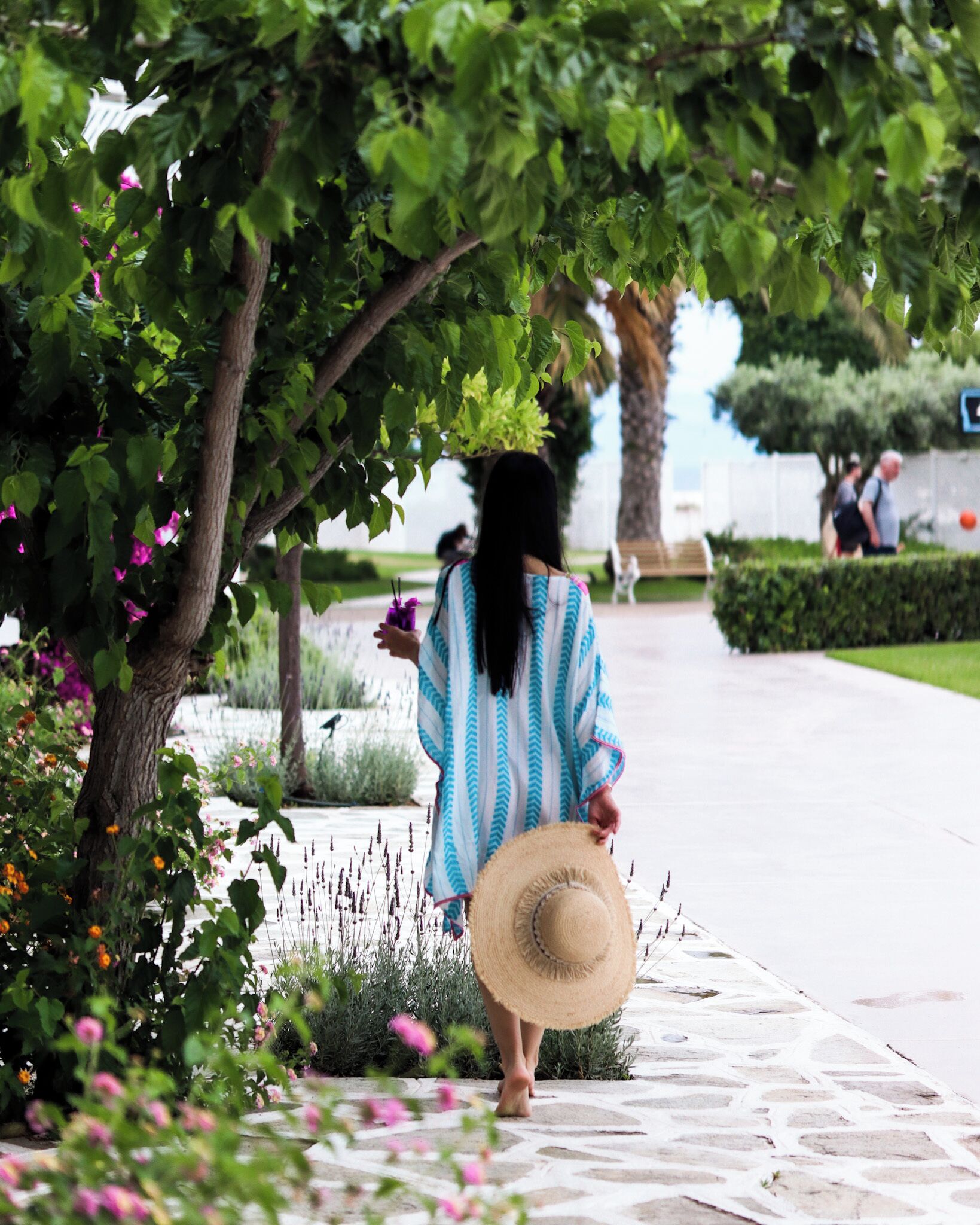 A person walking on a stone pathway surrounded by greenery and flowers.