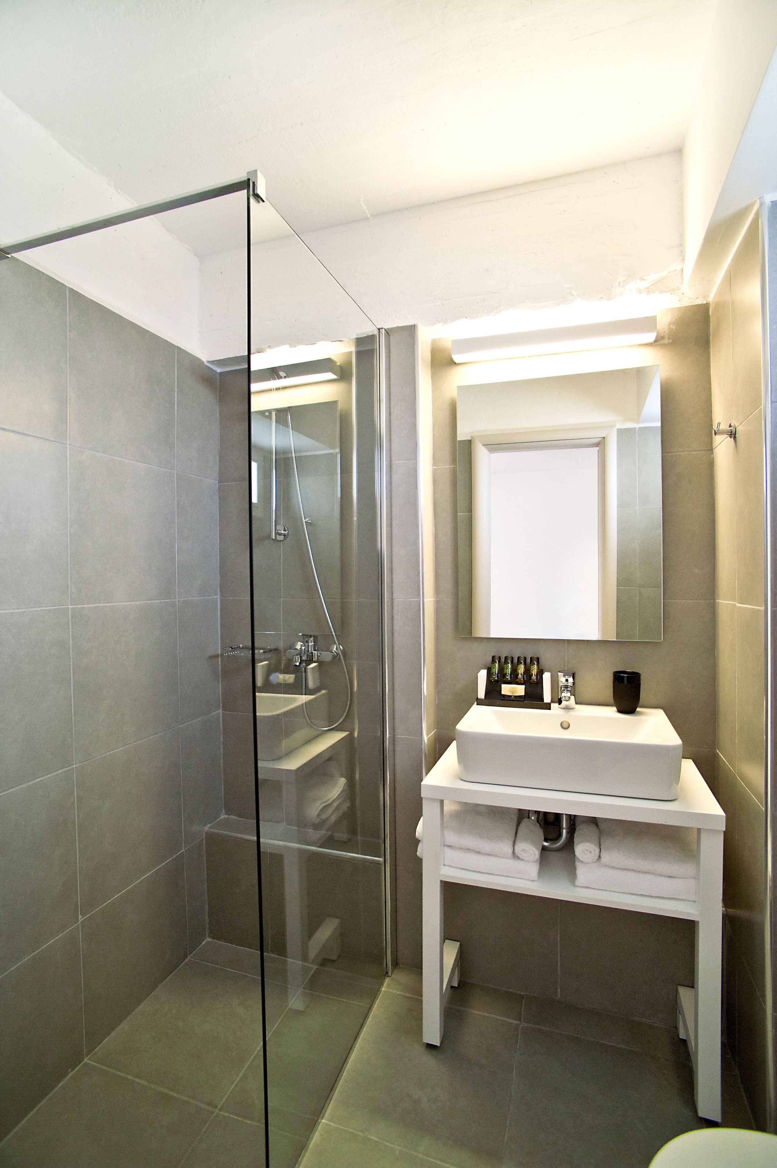 A modern bathroom with a glass shower enclosure, a white vanity with a mirror, and a tiled floor.
