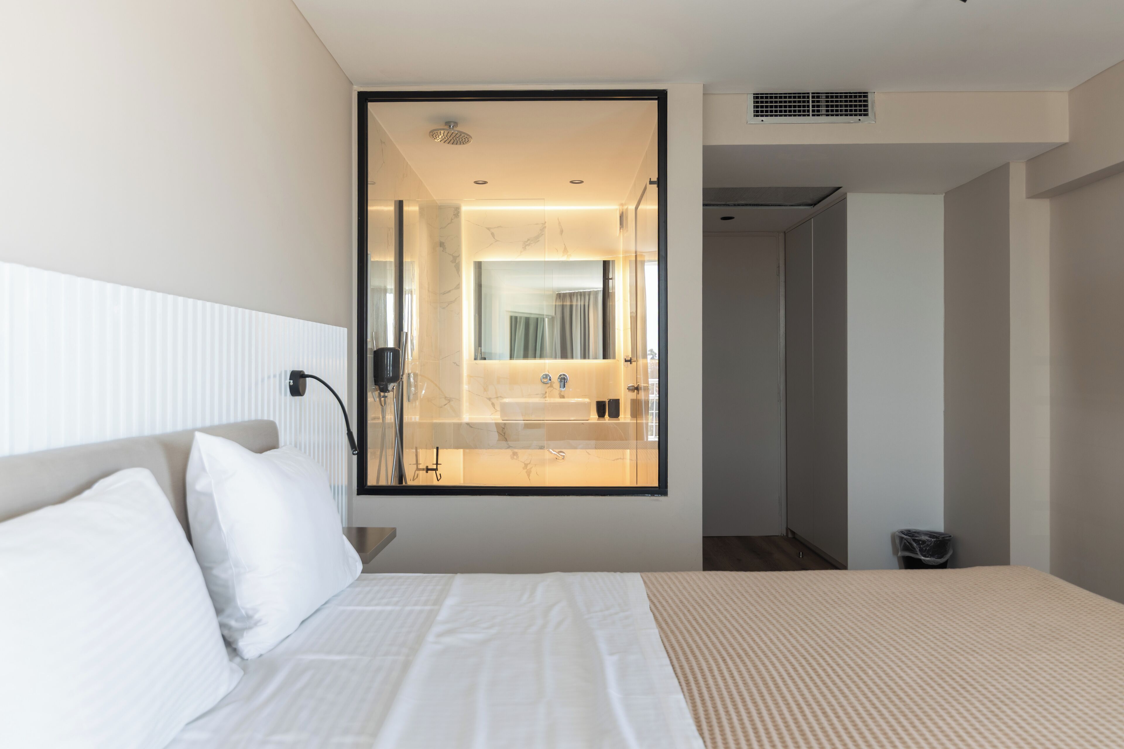 A modern hotel room with a large bed, a bedside table, a mirror, and a view of the bathroom.