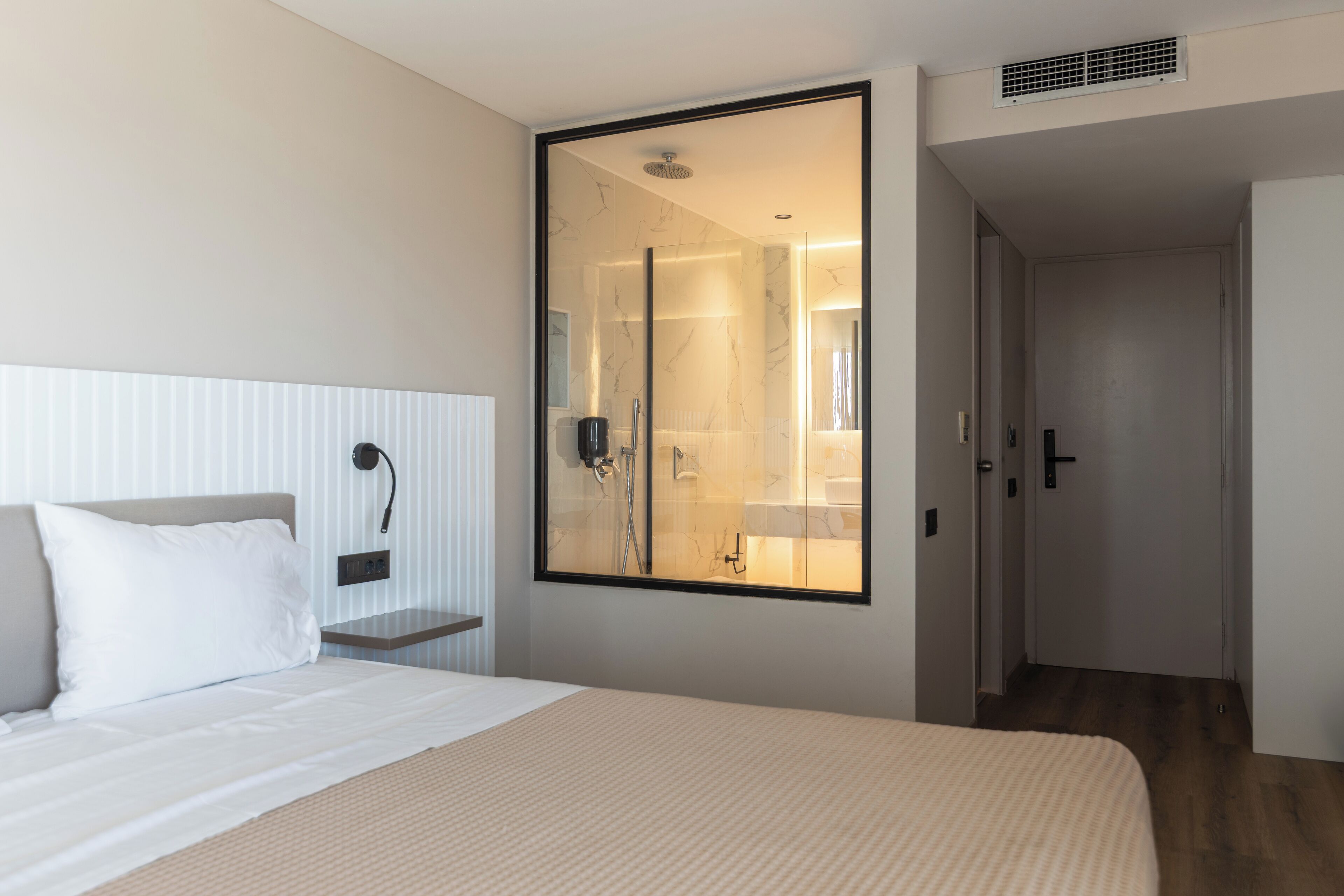Habitación de hotel con una cama grande, una mesita de noche, un espejo y vistas al baño.