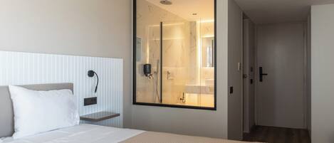Habitación de hotel con una cama grande, una mesita de noche, un espejo y vistas al baño.