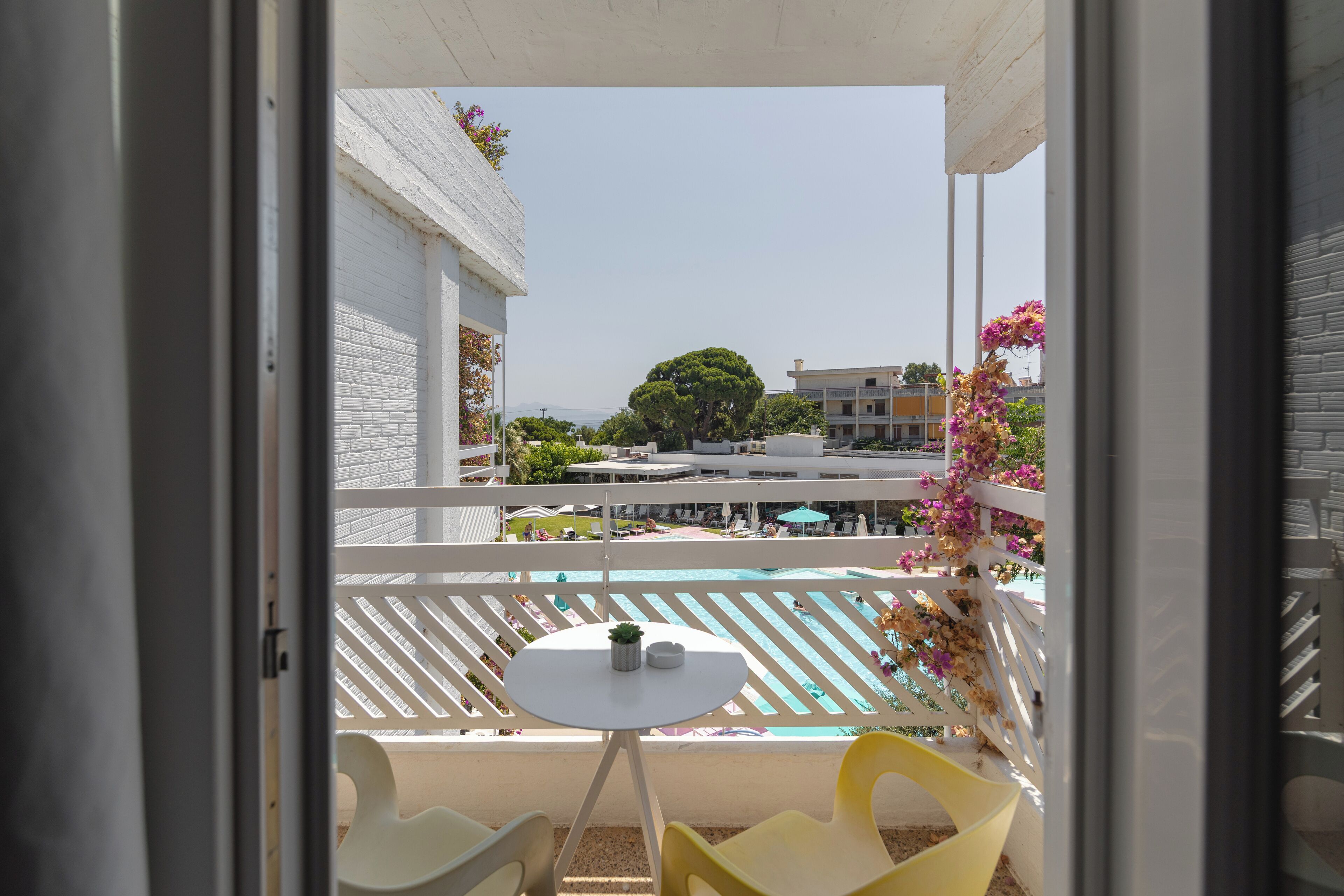Un balcon donnant sur la piscine, avec des meubles blancs et une petite table agrémentée d’une plante.