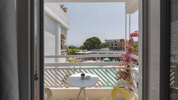A balcony with a pool view, white furniture, and a small table with a plant.