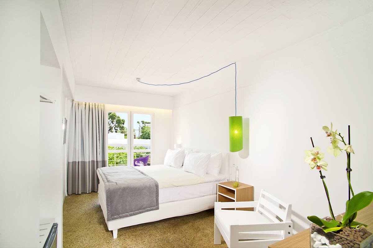 A modern bedroom with a bed, a bedside table, a chair, a window with curtains, and a potted orchid plant.