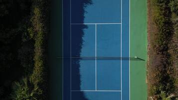 Vista aérea de una cancha de tenis rodeada de abundante vegetación.