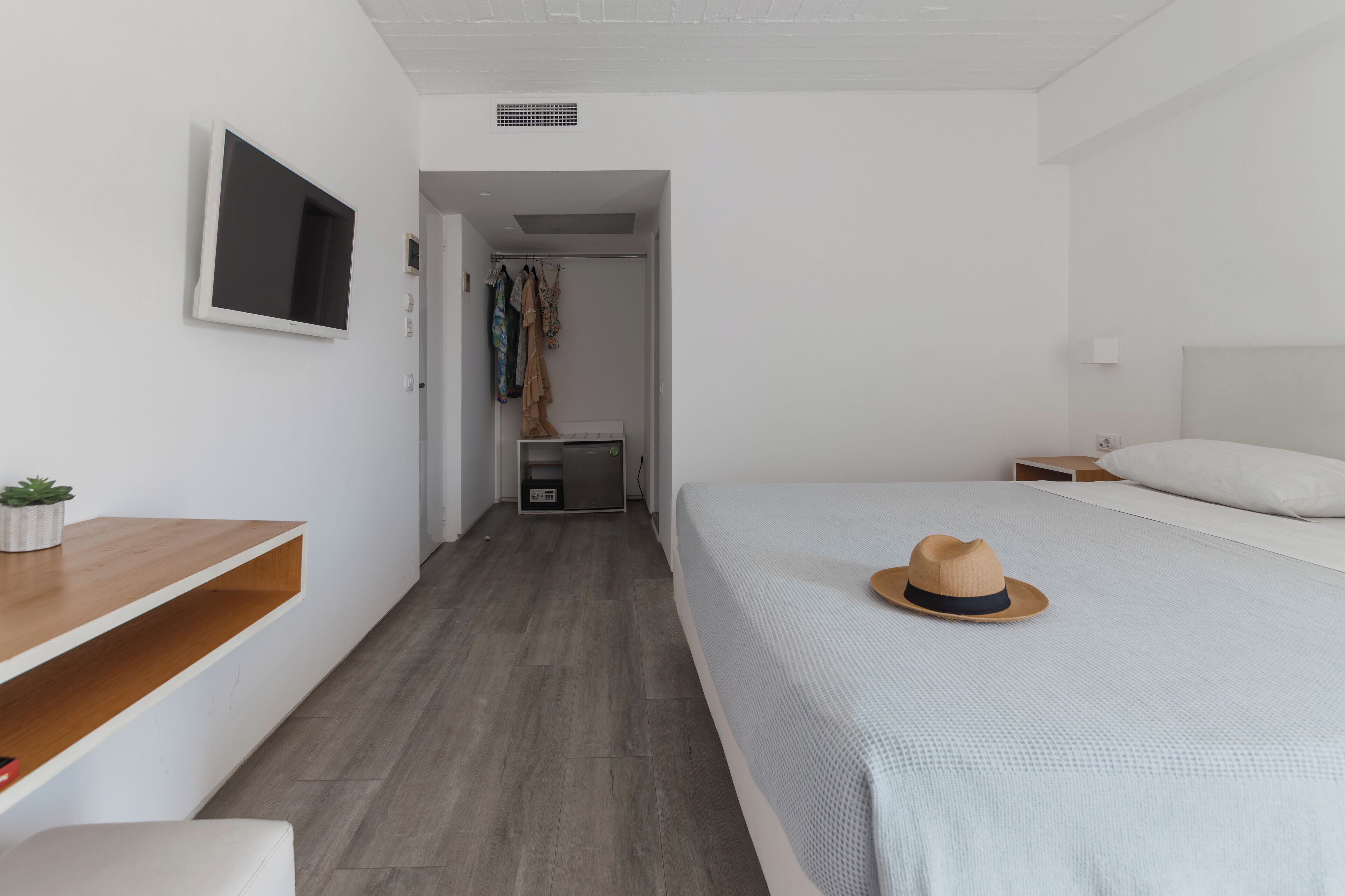 A modern hotel room with a bed, a desk, a TV, and a wardrobe.