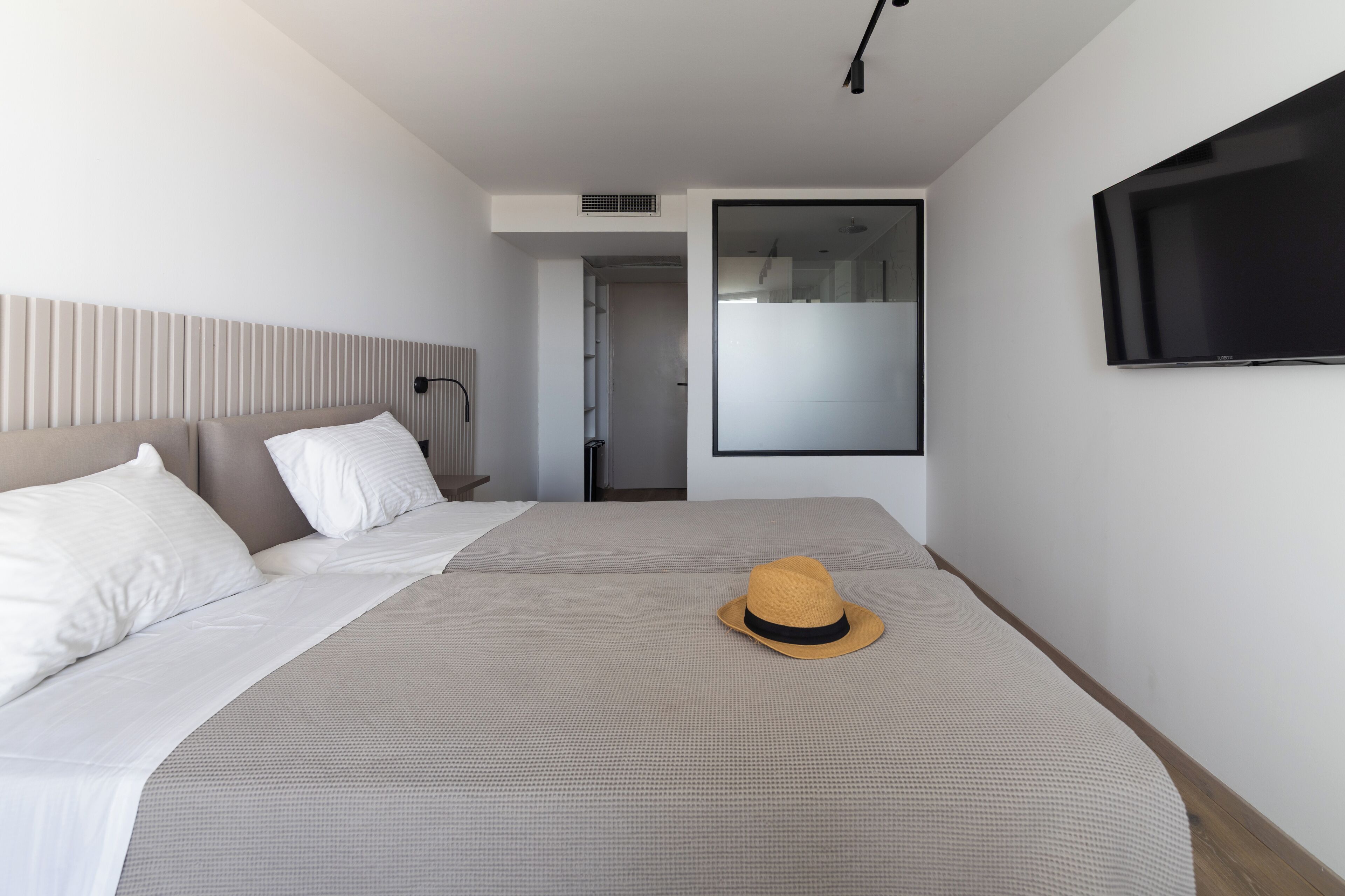 A modern hotel room with a large bed, a television mounted on the wall, and a sliding door leading to a bathroom.