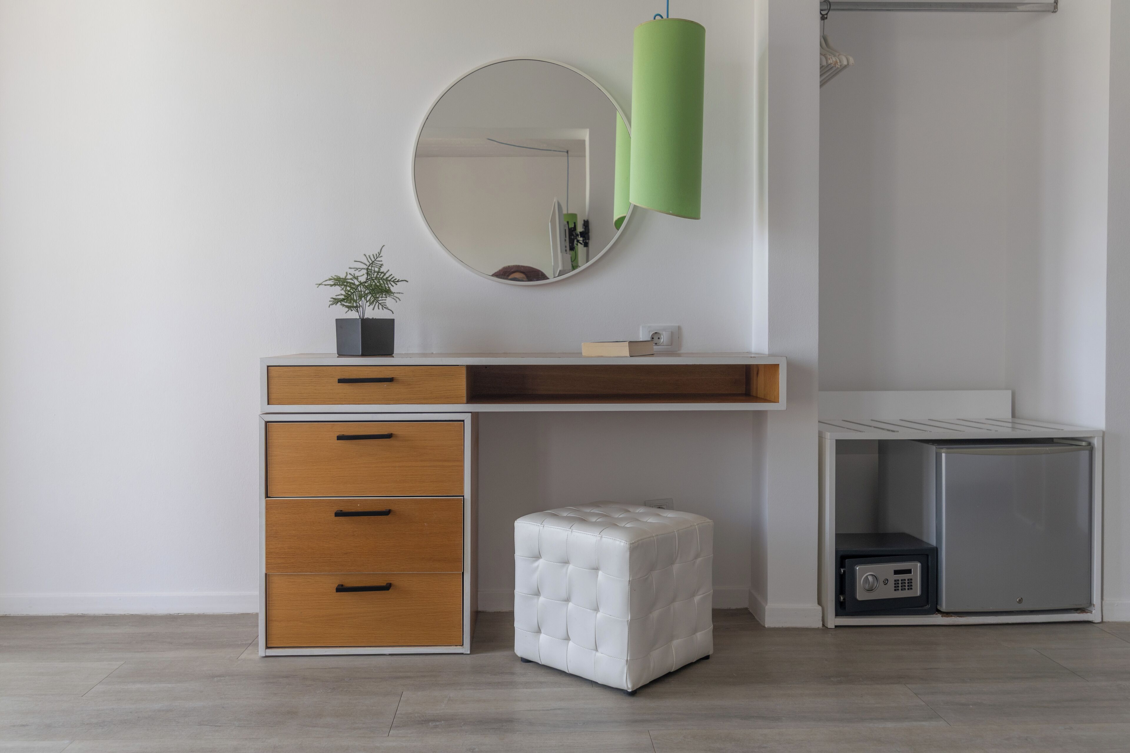 Een moderne badkamer met een wit wastafelmeubel, een ronde spiegel, een groene lamp, een kleine potplant en een inbouwkluis.