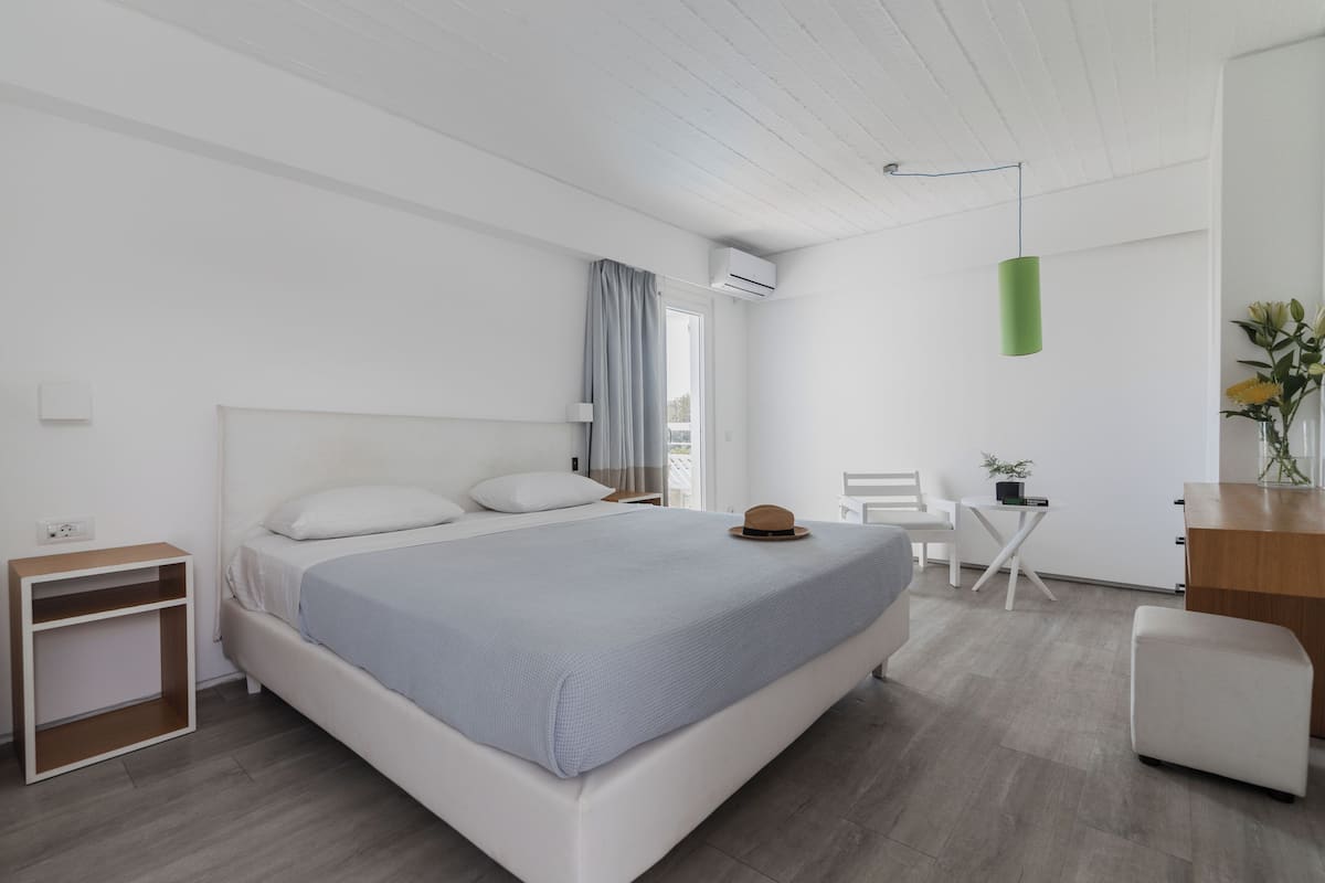 A modern bedroom with a large bed, a small desk, a chair, and a desk lamp.