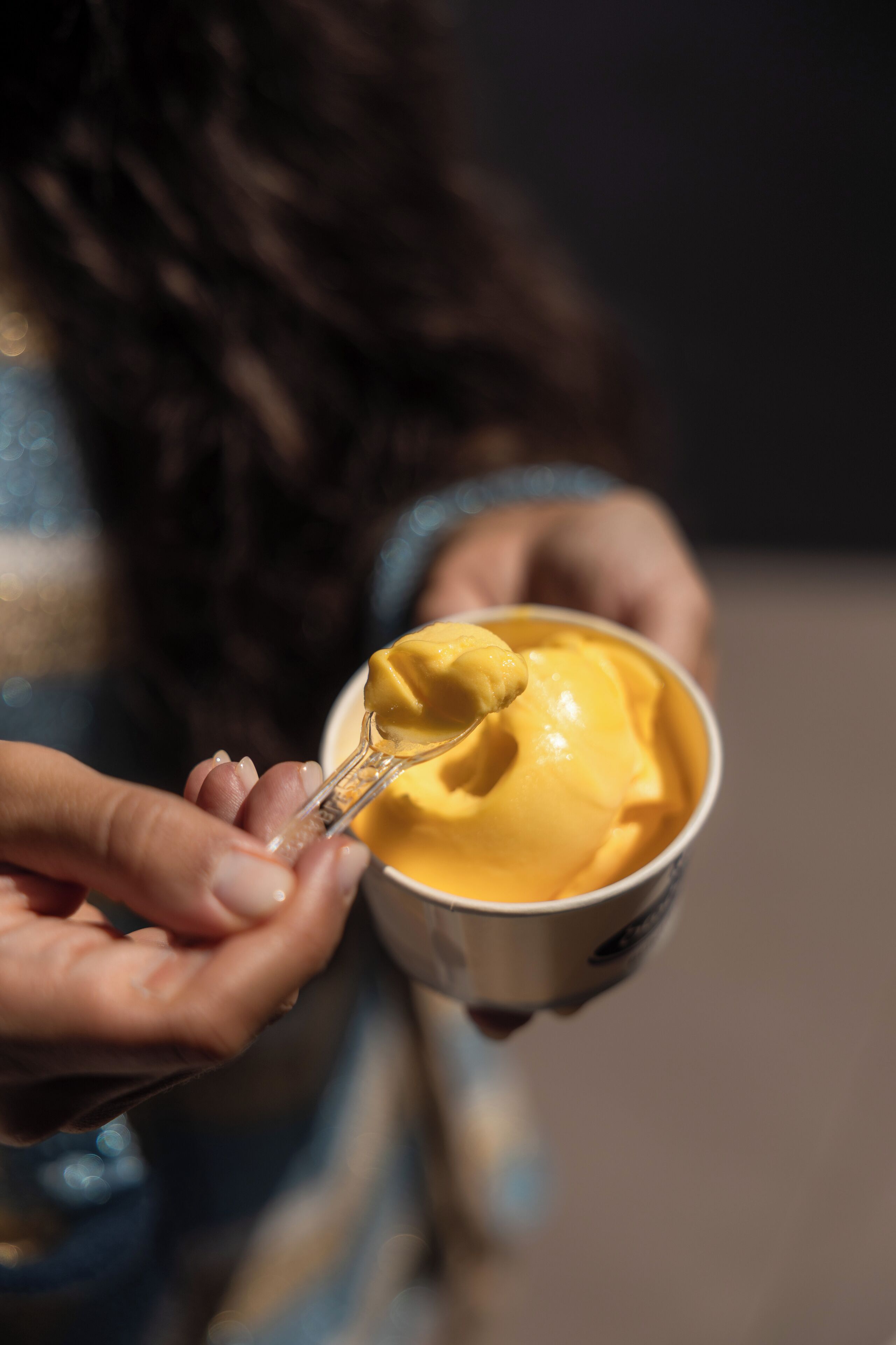 A person holding a bowl of yellow food with a spoon.