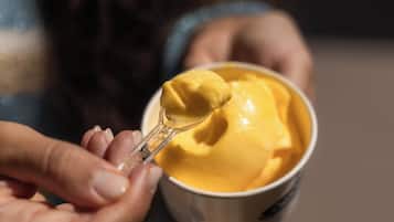 A person holding a bowl of yellow food with a spoon.