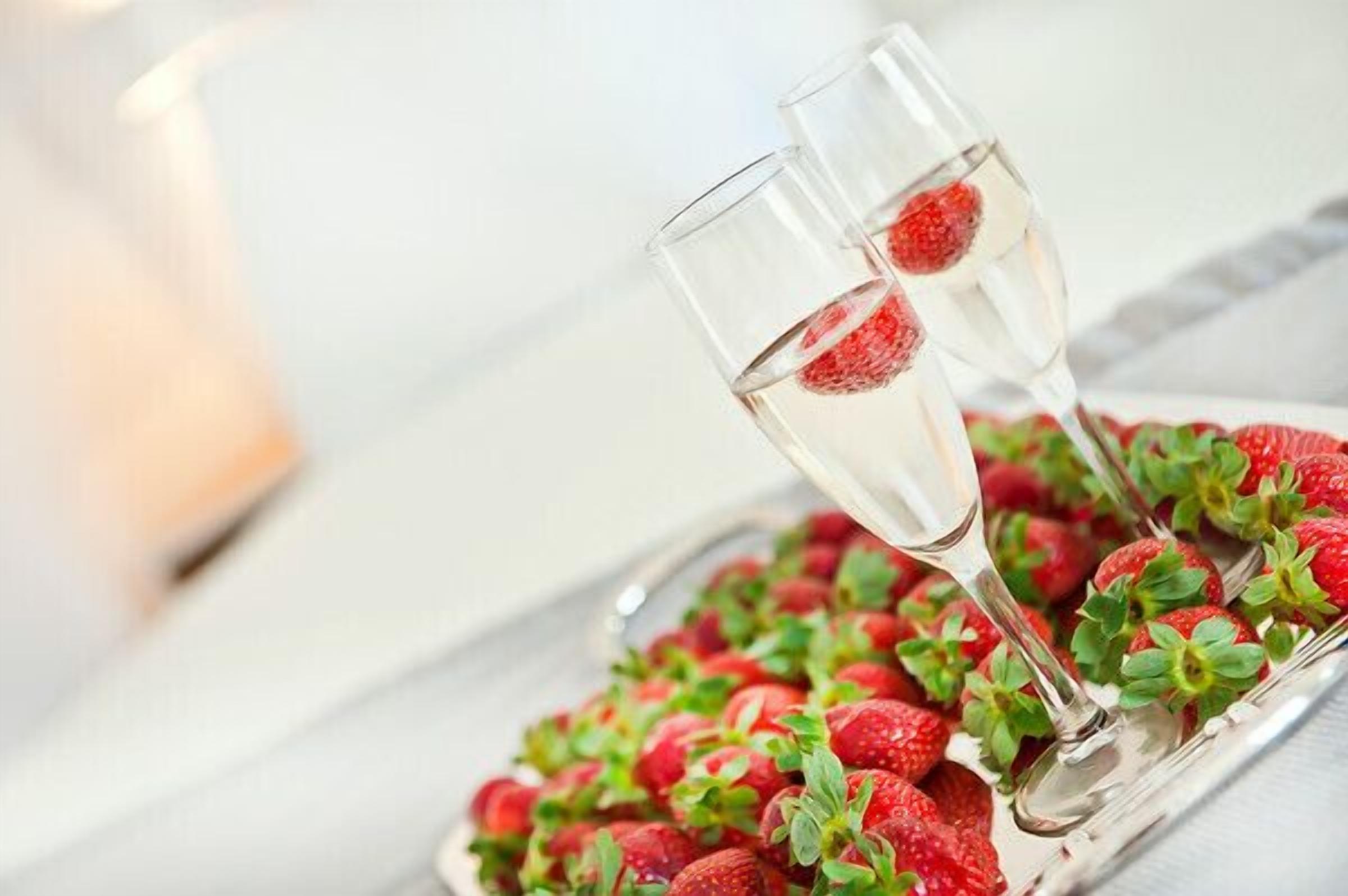Two champagne flutes with strawberries on the rim, placed on a tray of strawberries.