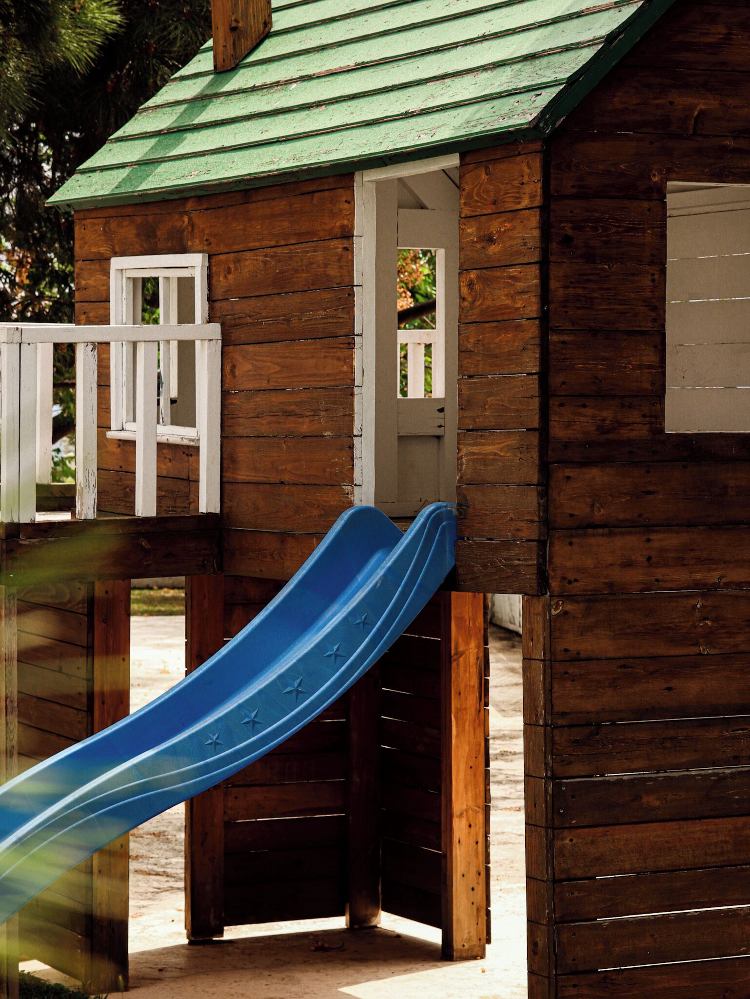 A wooden cabin with a green roof, a white door, and a blue slide.