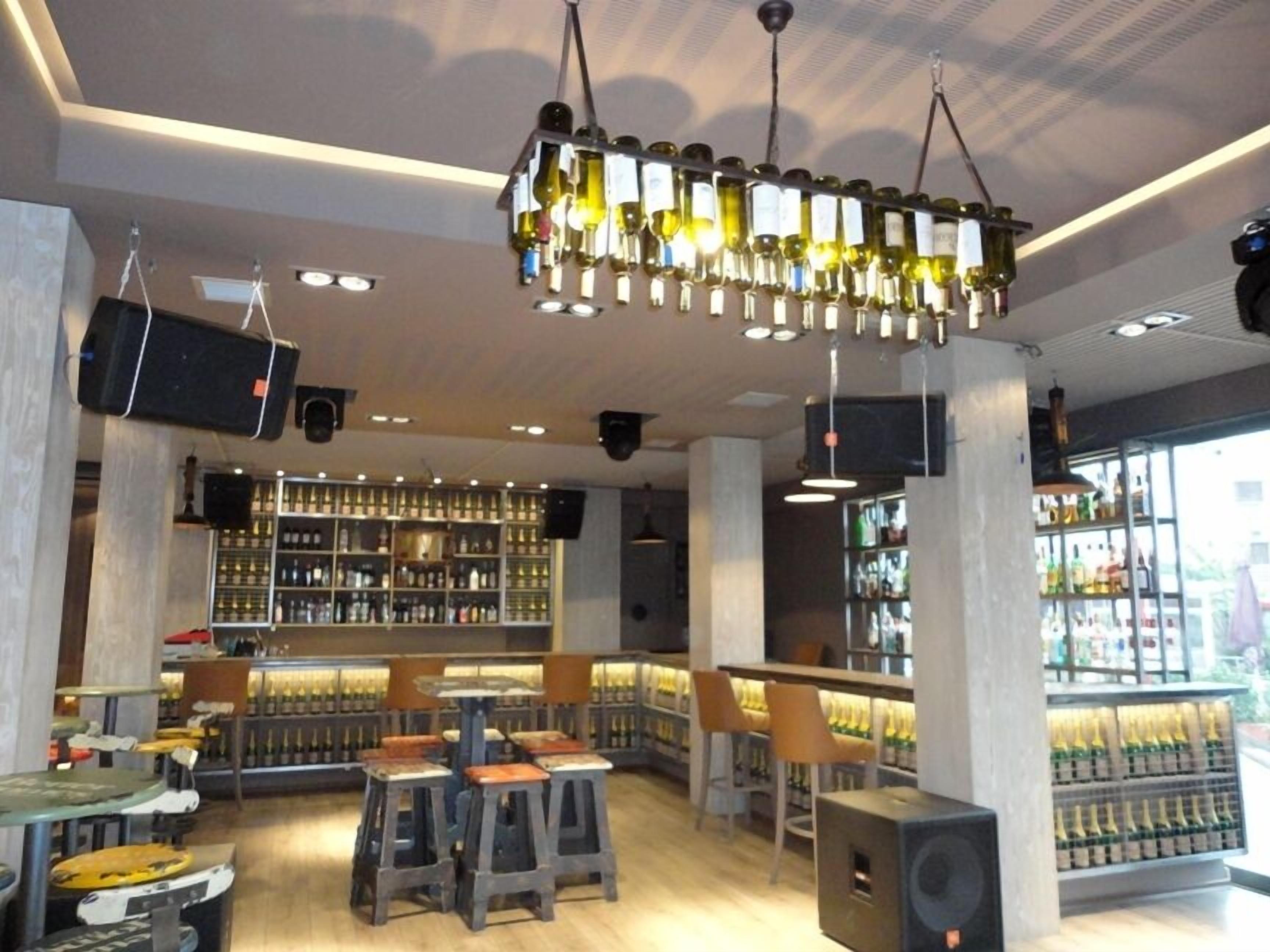 Un área de bar con taburetes, estantes llenos de botellas y una lámpara colgante.