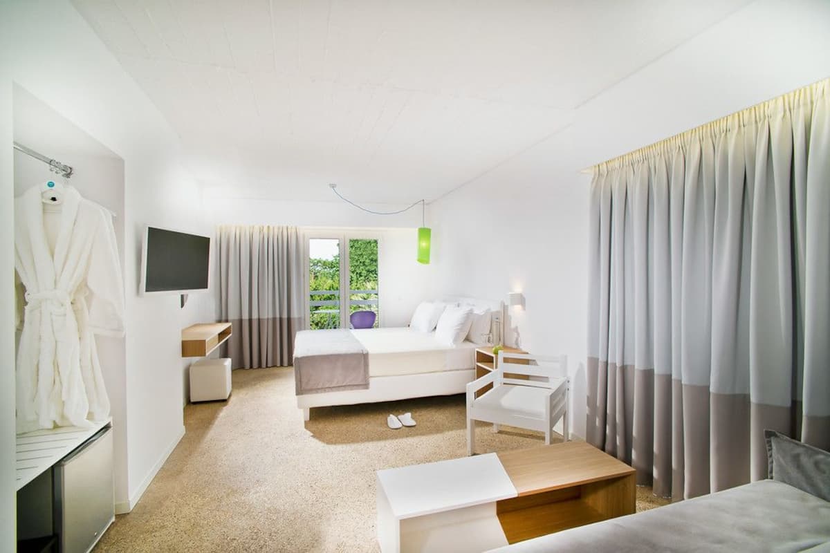 A modern hotel room with a bed, a desk, a chair, a TV, and a window with curtains.