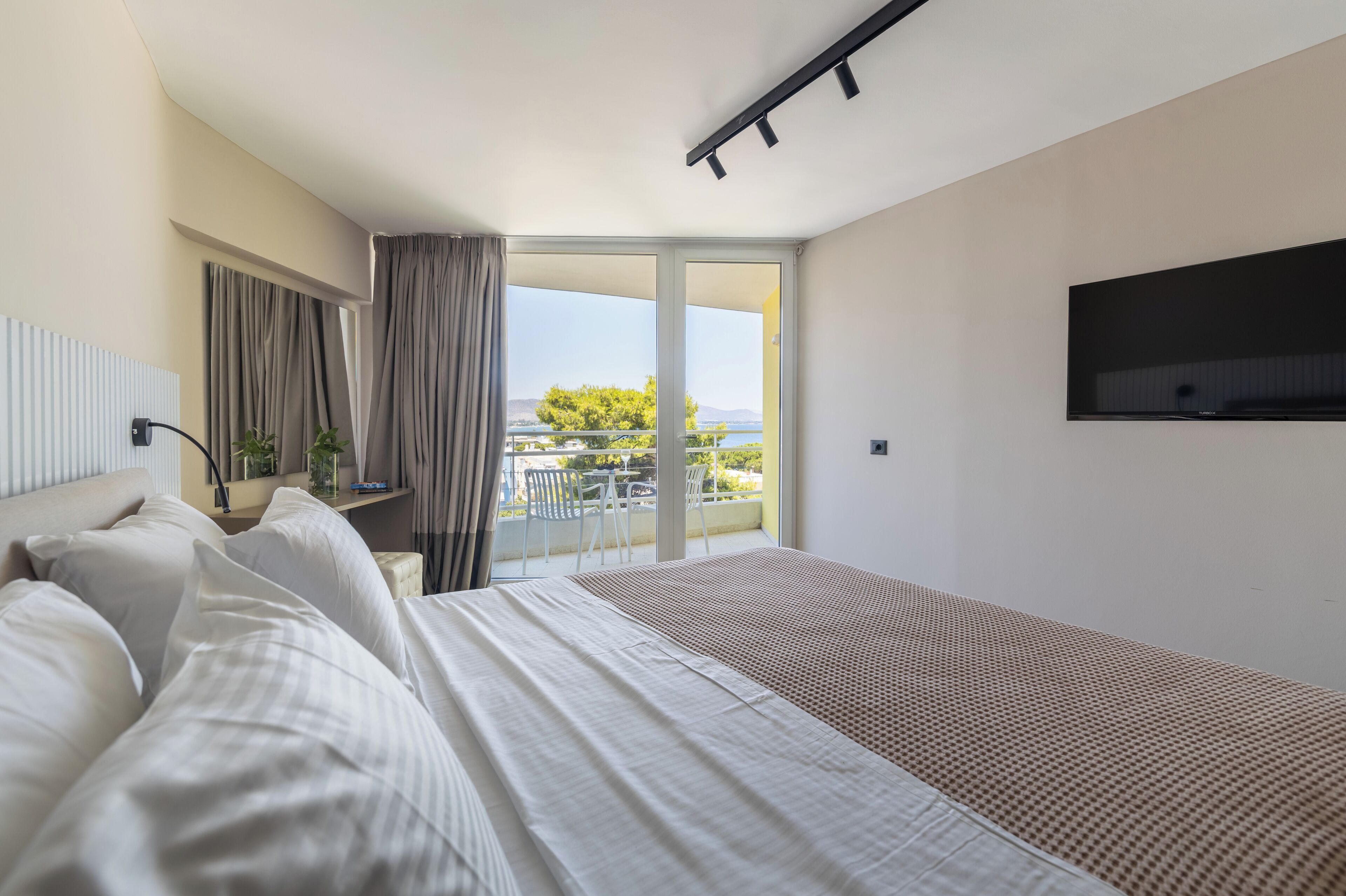 Habitació d'hotel amb un llit, televisió i un balcó que dona al mar.