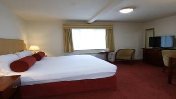 A hotel room with a large bed, a desk, a chair, a television, and a window with curtains.