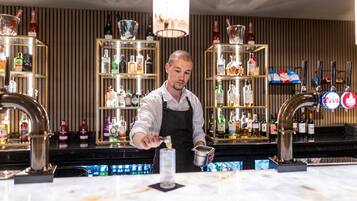 A bar area with shelves of liquor bottles, a bartender preparing a drink, and a bar counter with taps and a cash register.