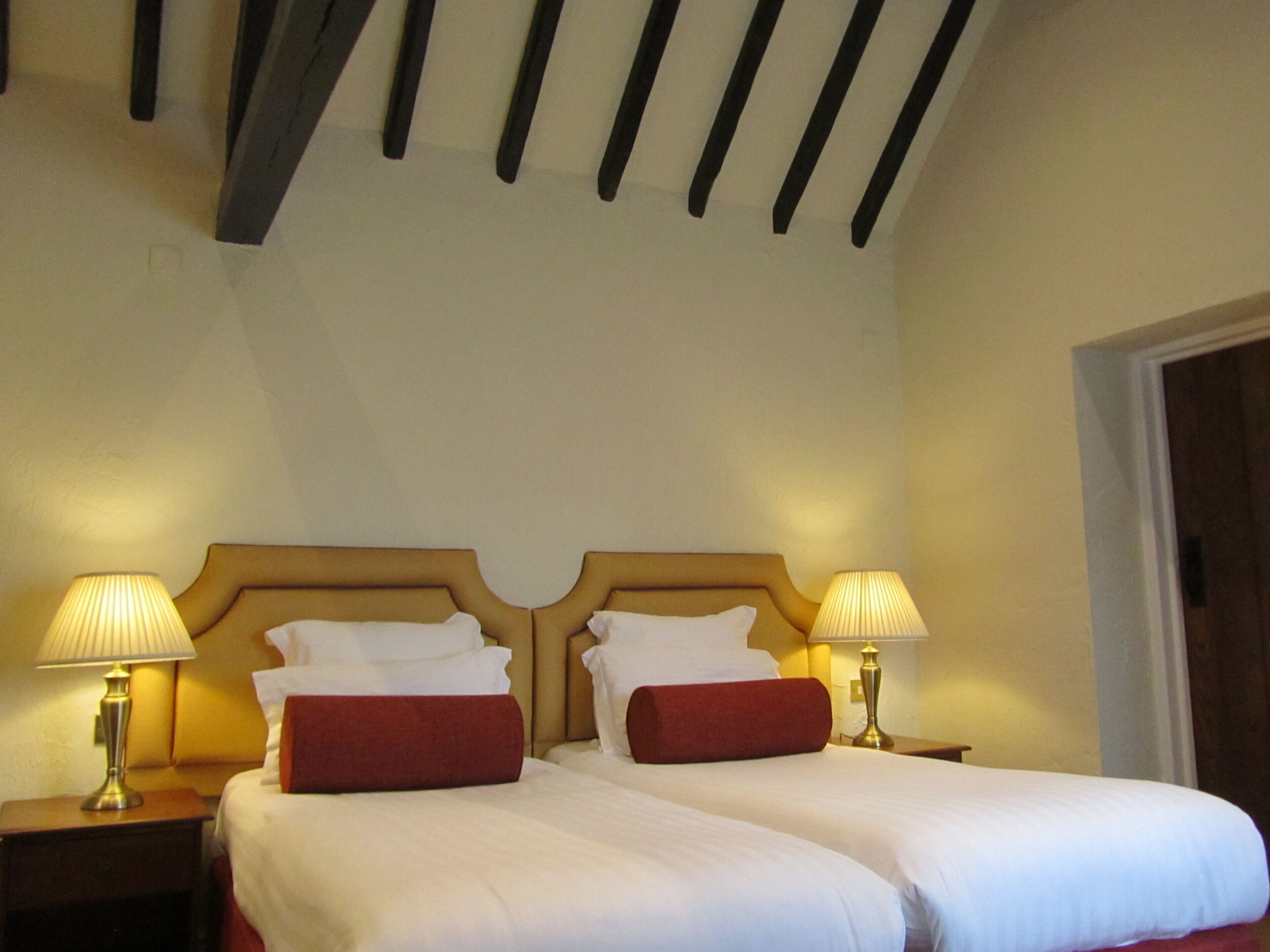 A double bed with white linens and red pillows, two bedside lamps, and a wooden headboard.