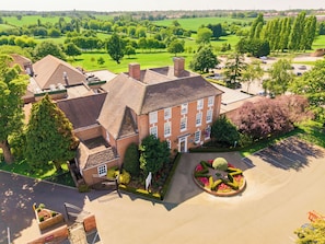 Un grand bâtiment en briques, doté de nombreuses fenêtres, entouré d’une végétation luxuriante et d’une pelouse bien entretenue.