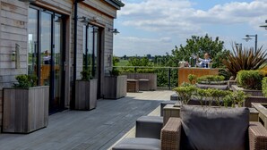 A modern outdoor patio with wooden flooring, built-in planters, and wicker furniture. -  Windmill Village Hotel, Golf Club & Spa, BW Signature Collection (Coventry)