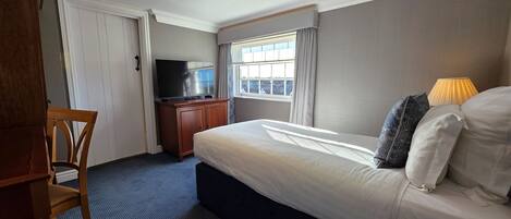 A hotel room with a bed, a TV on a wooden cabinet, a window with curtains, and a chair.