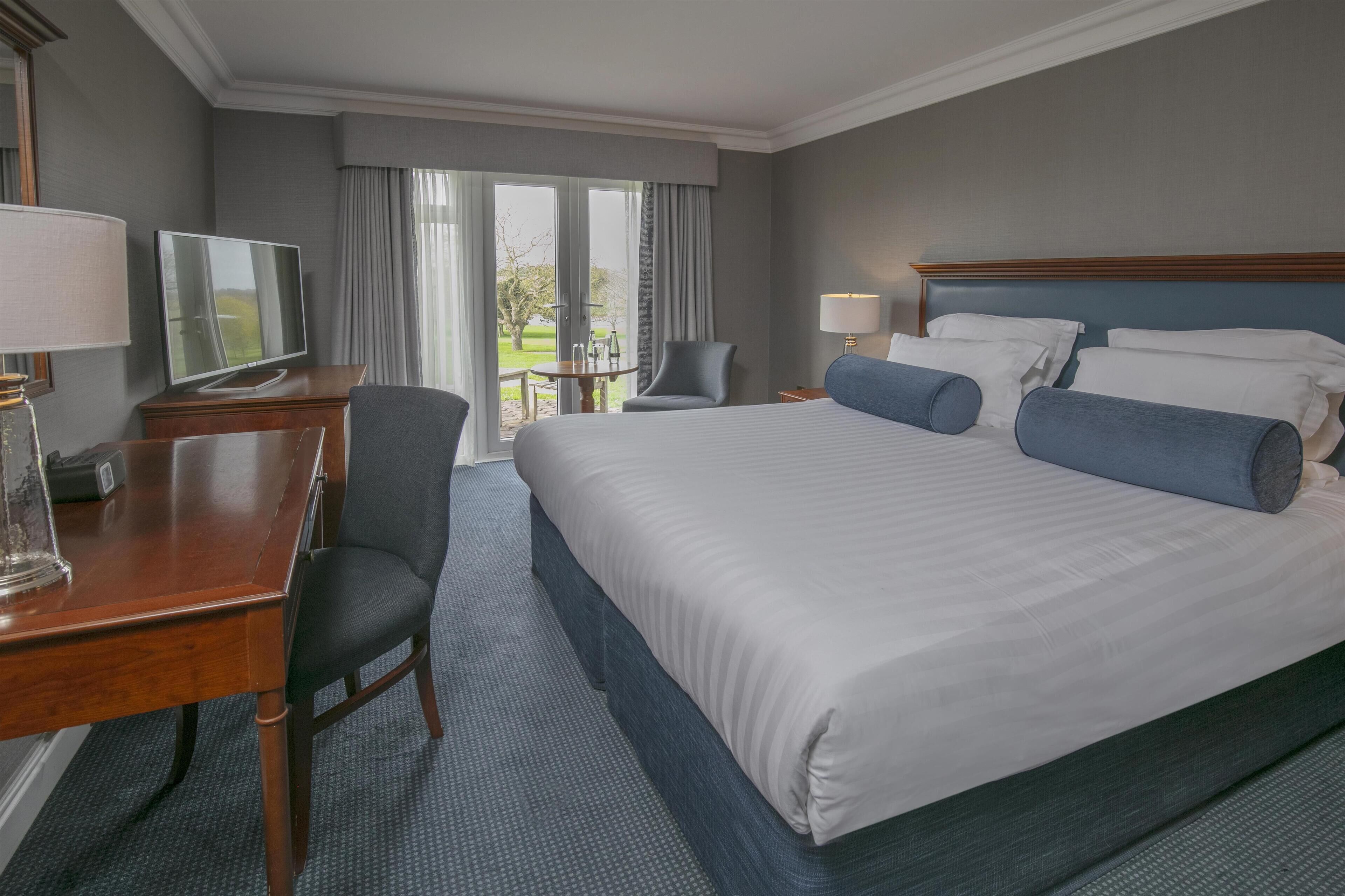 A hotel room with a large bed, a desk with a TV, a chair, and a view of the outdoors.