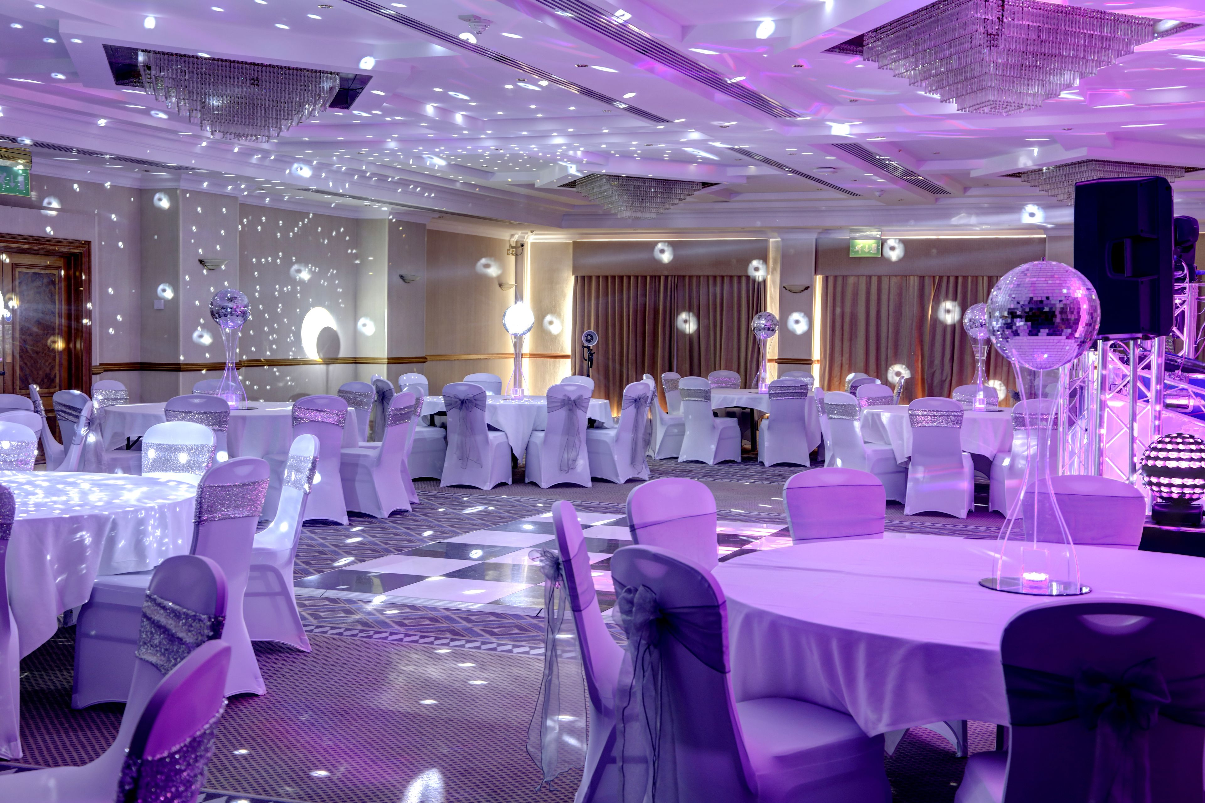 A banquet hall with round tables and chairs, each with a white tablecloth and a bow on the chair.